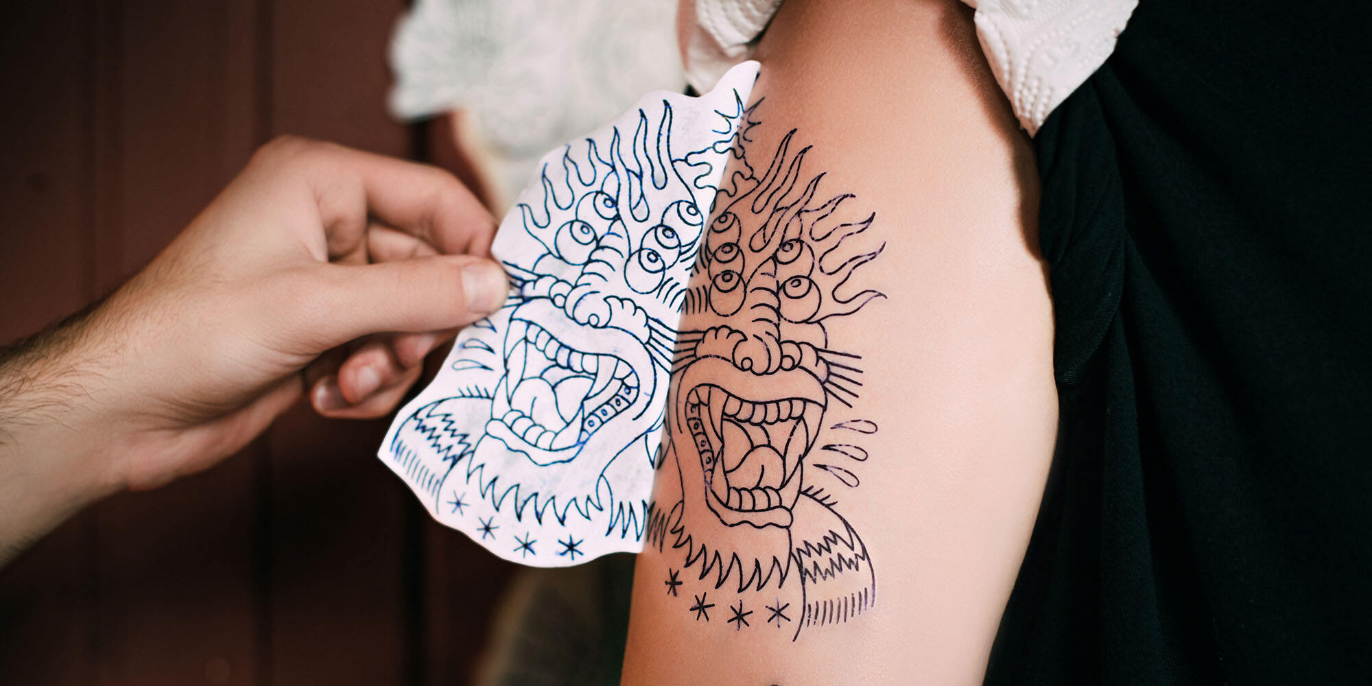 cropped shot of tattoo artist transferring tattoo sketch on shoulder in tattoo salon